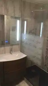 Rénovation de salle de bain avec douche vitrée, carrelage texturé et meuble de rangement en bois.