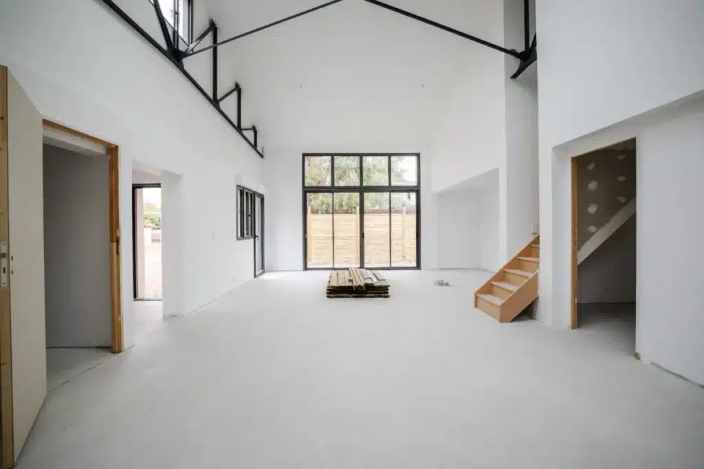 Vue d'une pièce en cours de rénovation avec un sol brut, des murs blancs et des ouvertures vitrées, réalisée par une entreprise de rénovation à Bordeaux.